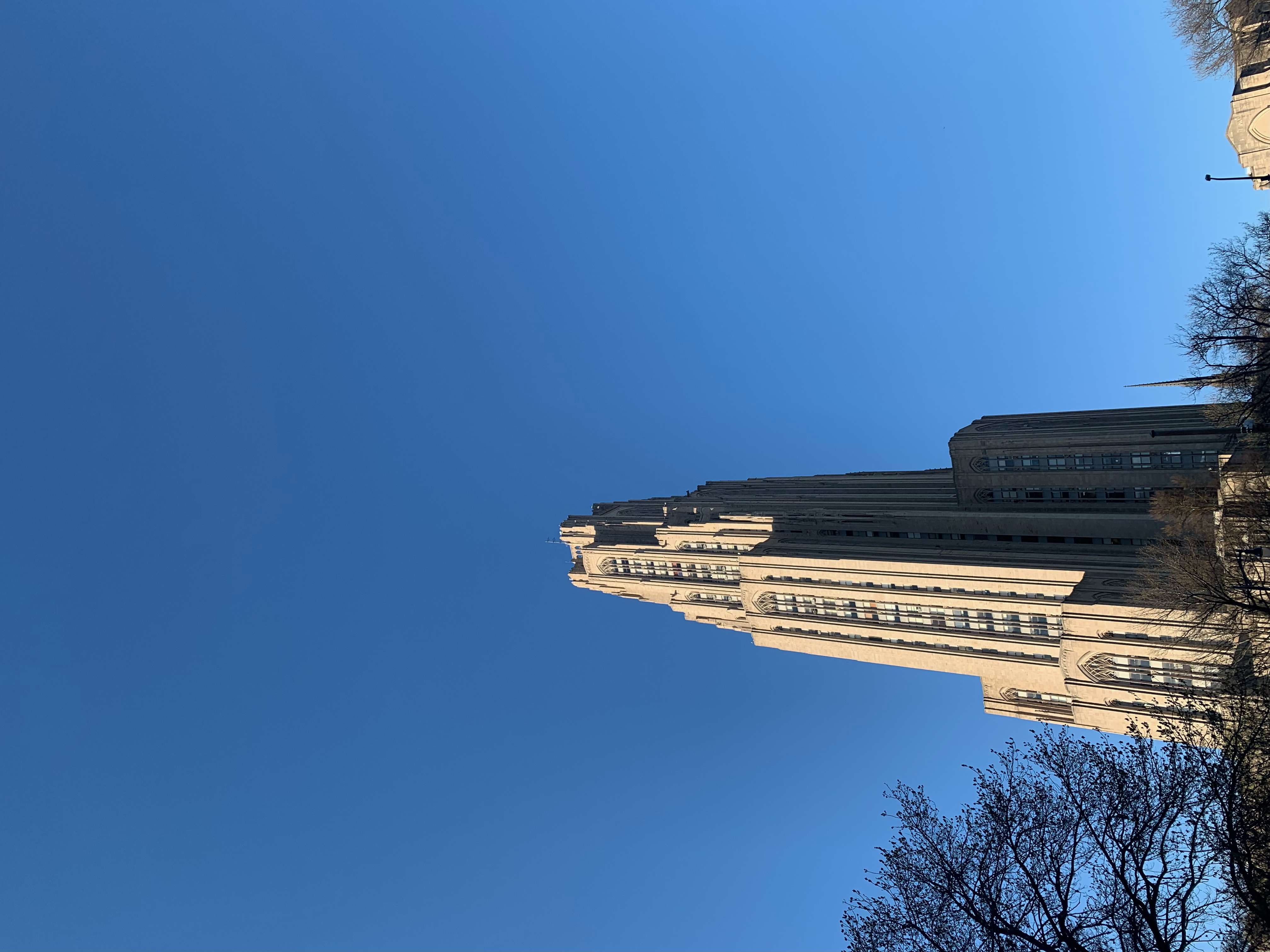 Sun hitting one side of art deco style Cathedral of Learning. Blue, cloudless sky background.