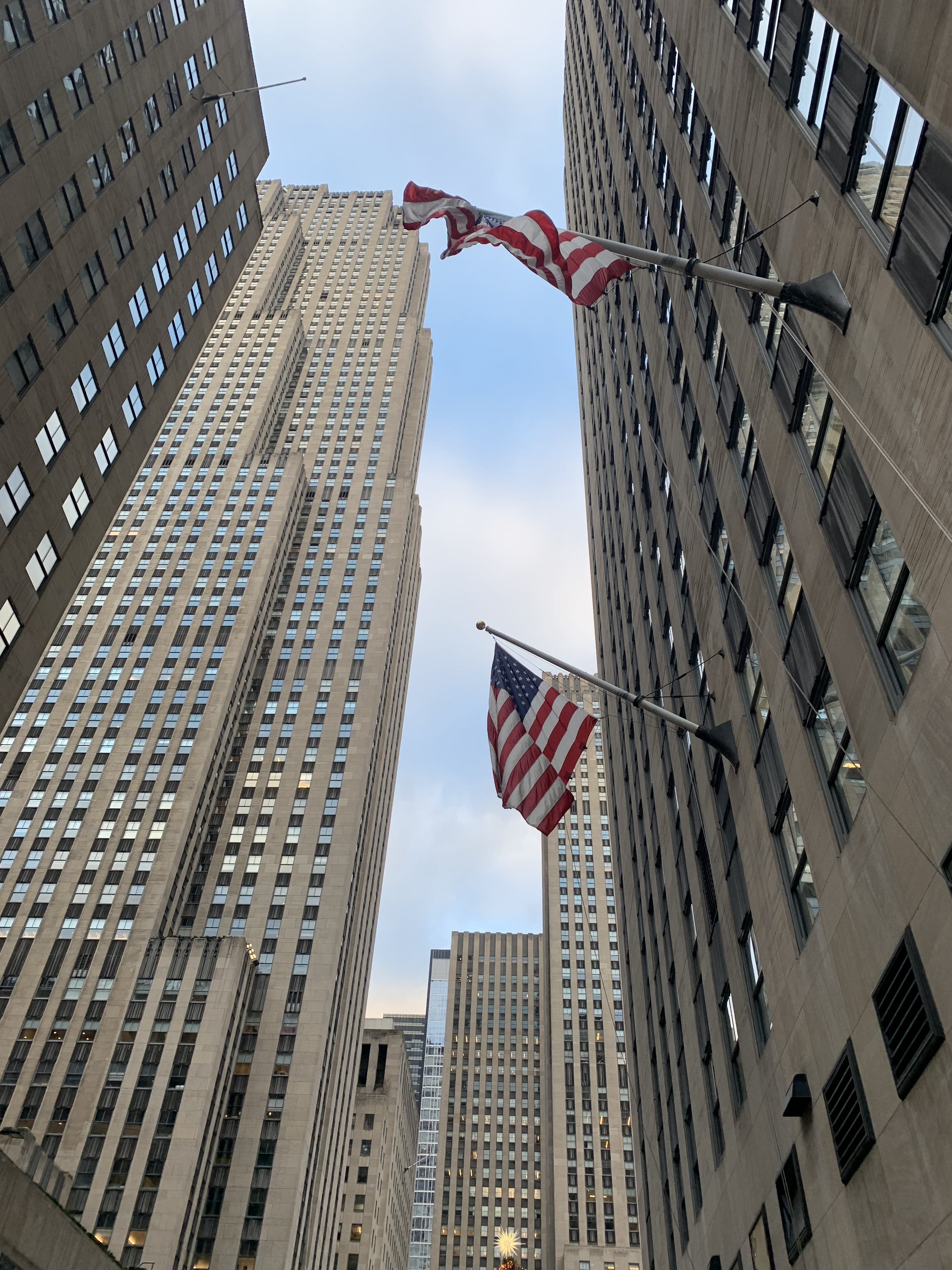 View from street looking up at concrete skyscrapers with 
                rectangular windows. American flags waking on the building to the right.