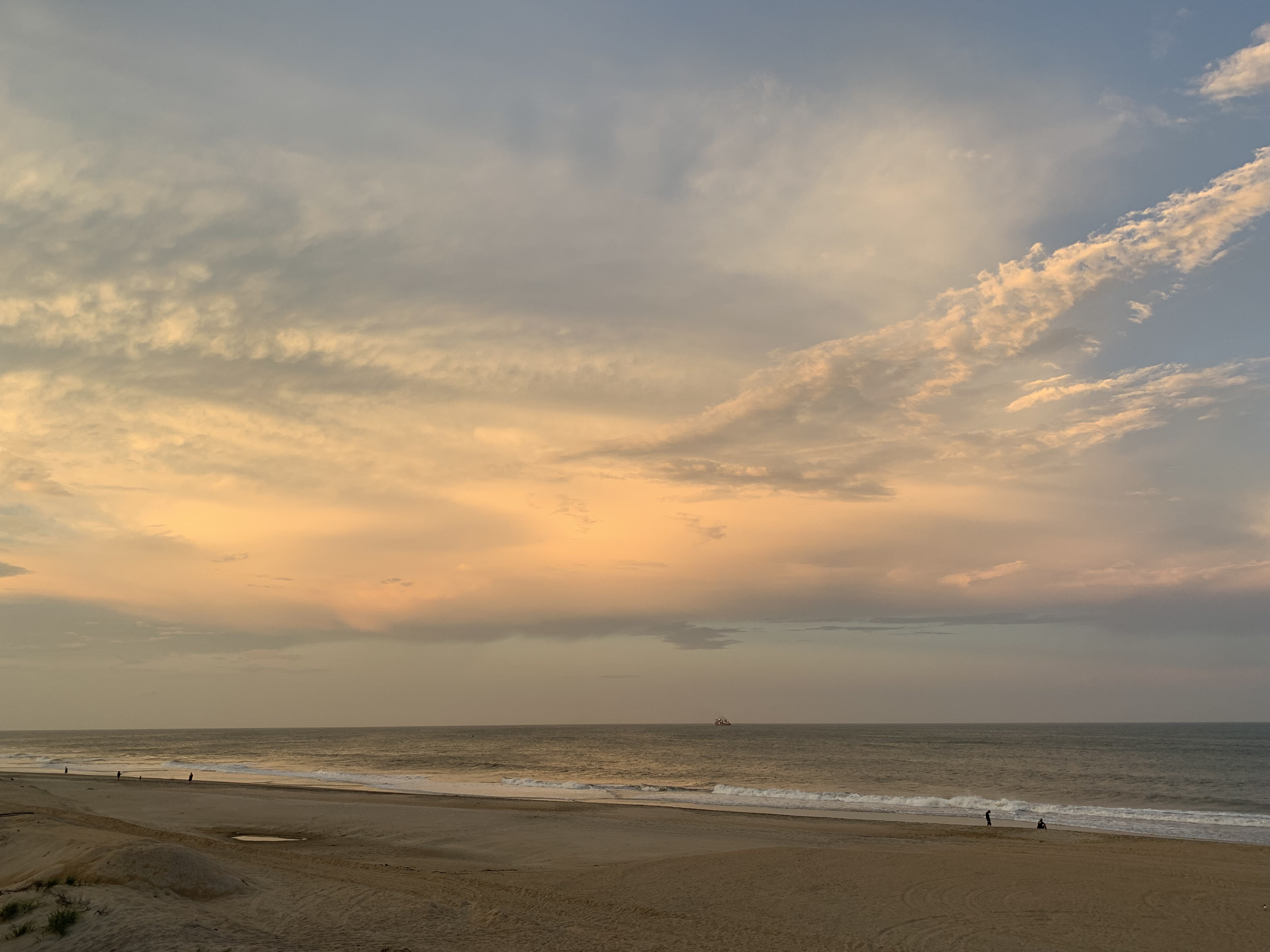 Beach at dusk. Sun turning clouds shades of orange against
                    blue sky. Sand and calm ocean in foreground.