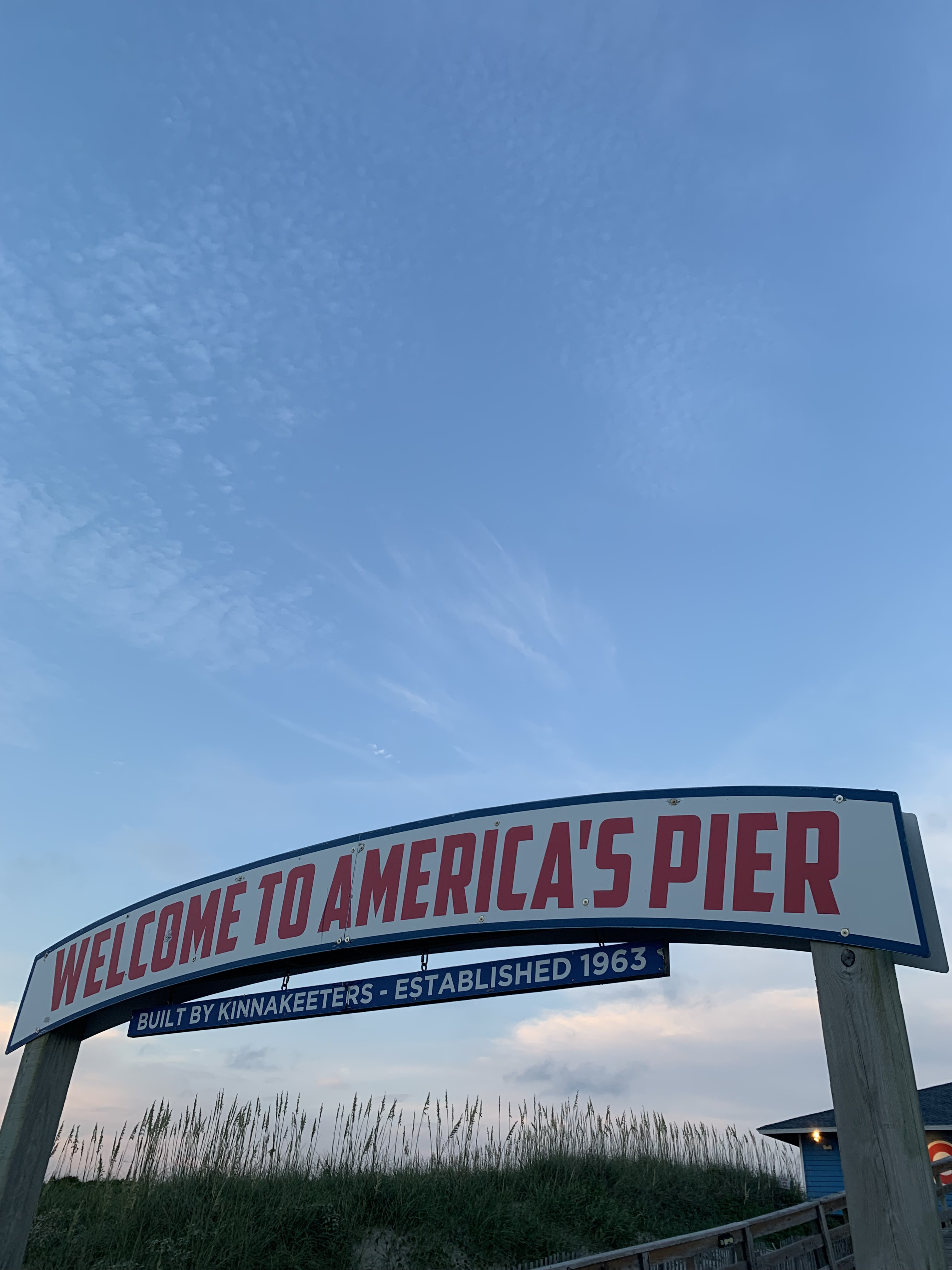 Blue sky with few wispy clouds. Large curved sign in foreground
                    that reads "Welcome to Americas Pier."