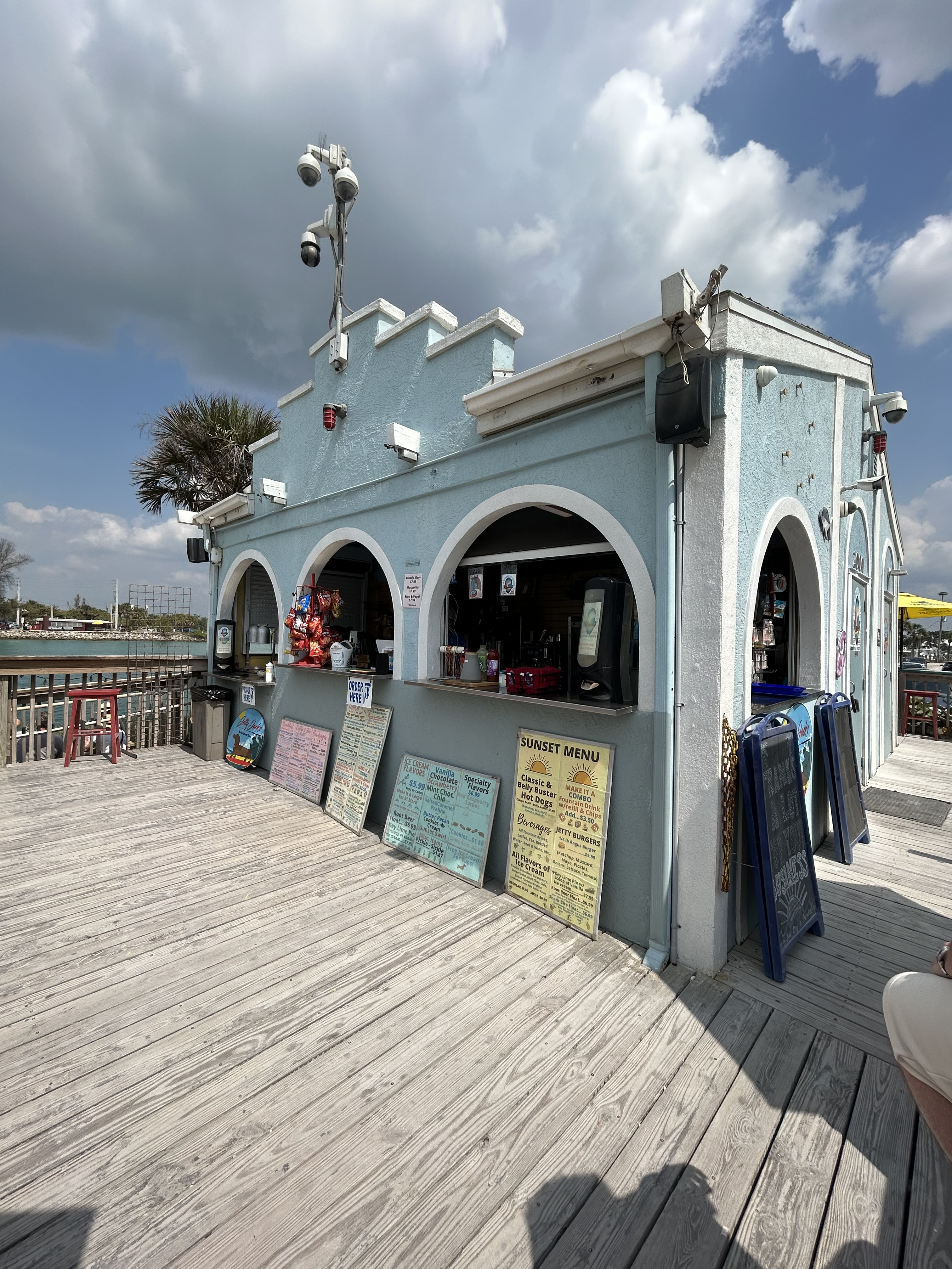 Light teal concrete building lined with white trim.
                Wooden deck around building. Colorful menu signs propped against
                building.